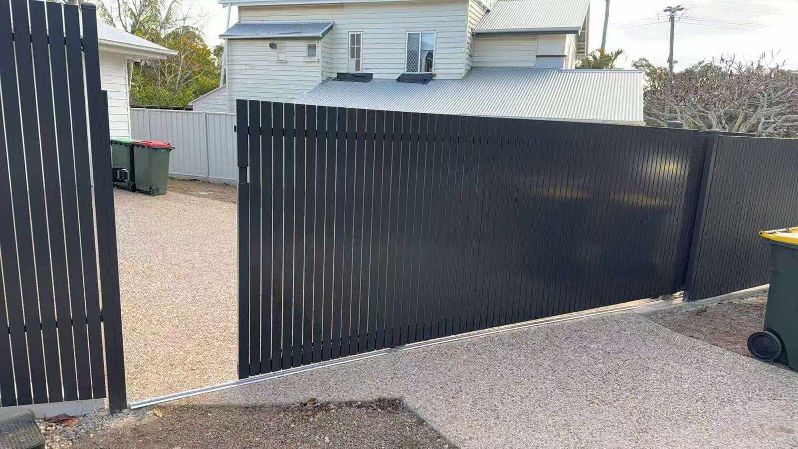 Dark grey aluminium vertical picket sliding driveway gate across a gravel driveway