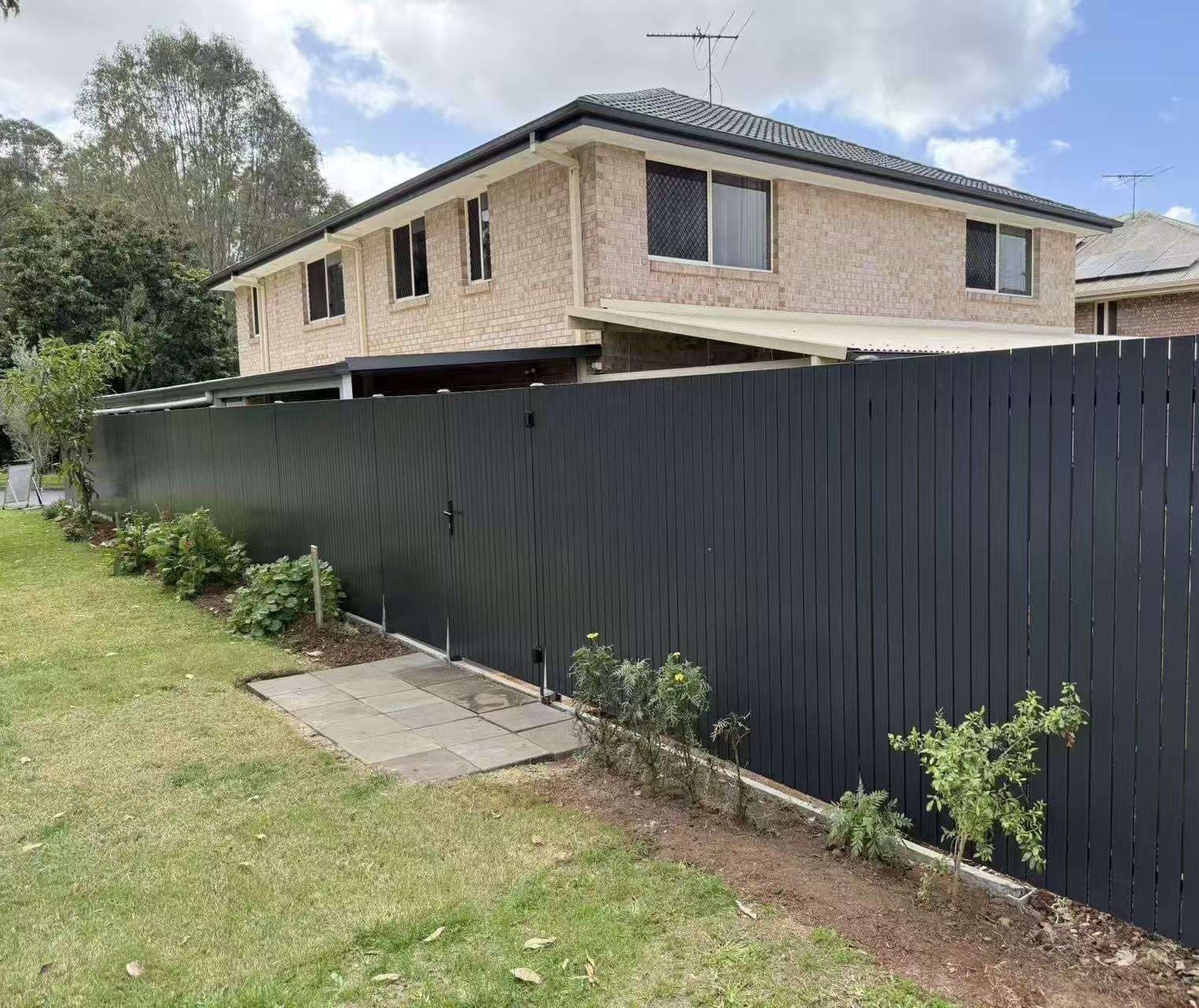 Dark grey aluminium vertical picket fence and pedestrian gate beside a garden bed at a brick two-storey home