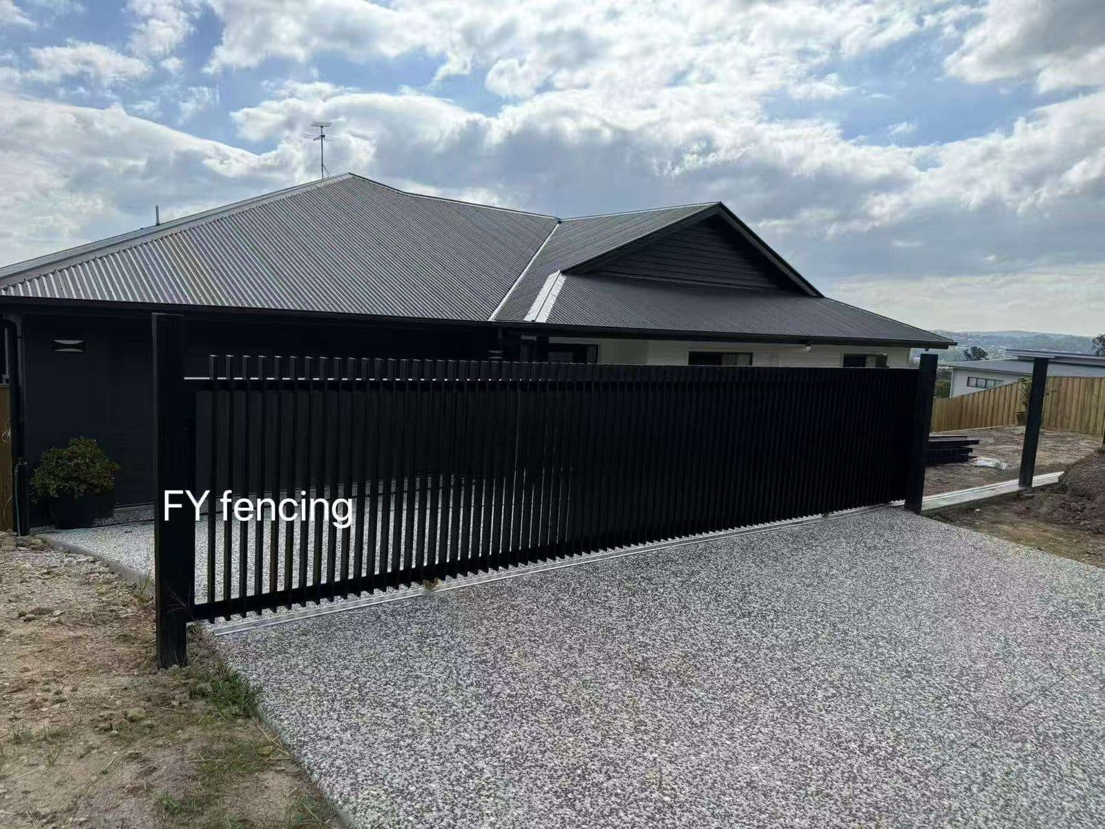 Black aluminium welded vertical blade sliding driveway gate across an aggregate driveway at a new home