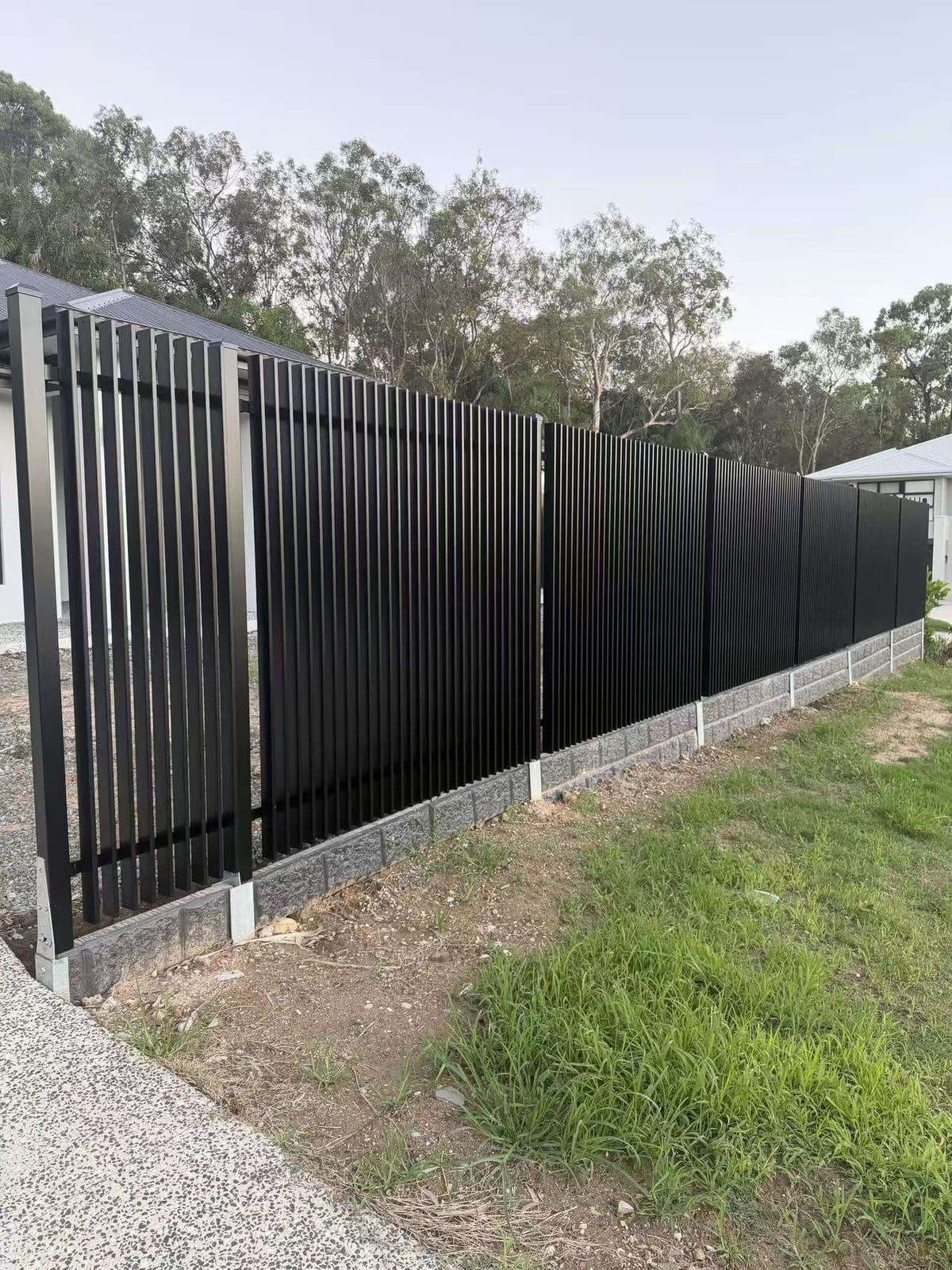 Black aluminium welded vertical blade fence on a split-face block retaining wall at a Brisbane home