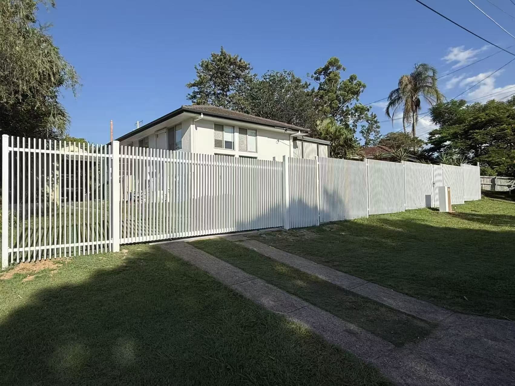 White aluminium welded vertical blade fence and sliding driveway gate along a lawn front boundary
