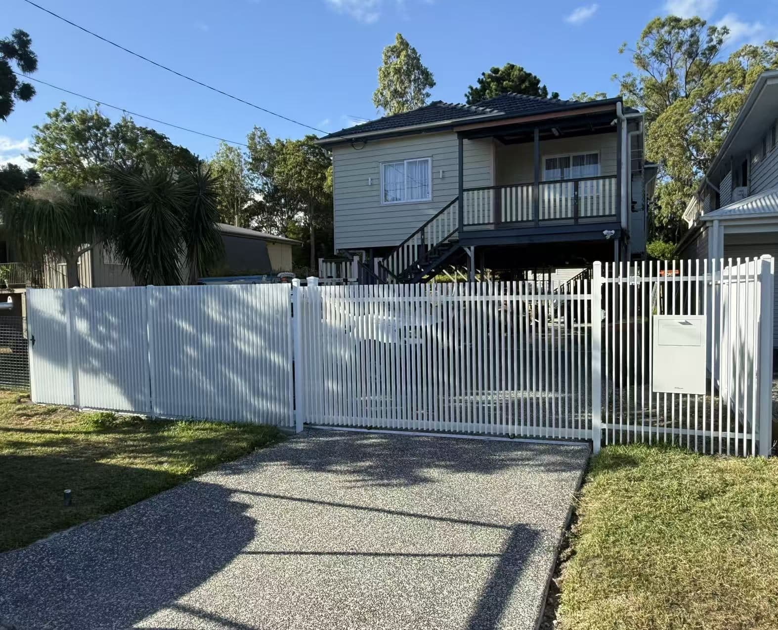 White aluminium welded vertical blade sliding driveway gate, fence and letterbox panel across an aggregate driveway