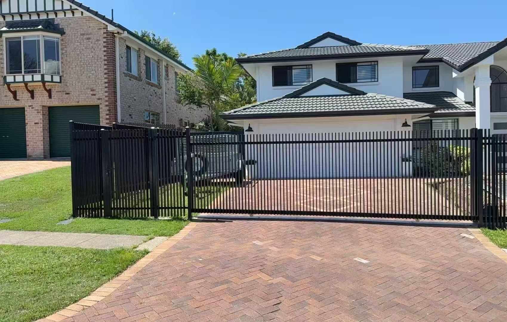 Black aluminium welded vertical blade sliding driveway gate and fence across a herringbone paved driveway