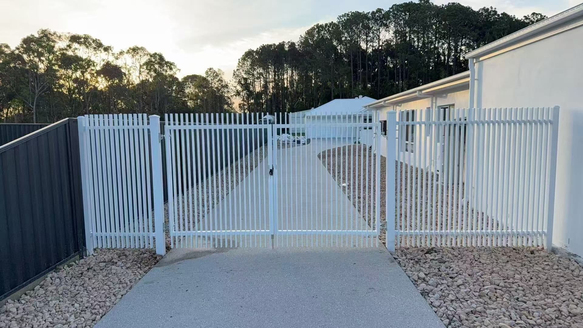 White aluminium welded vertical blade double swing gate and fence across a concrete side driveway