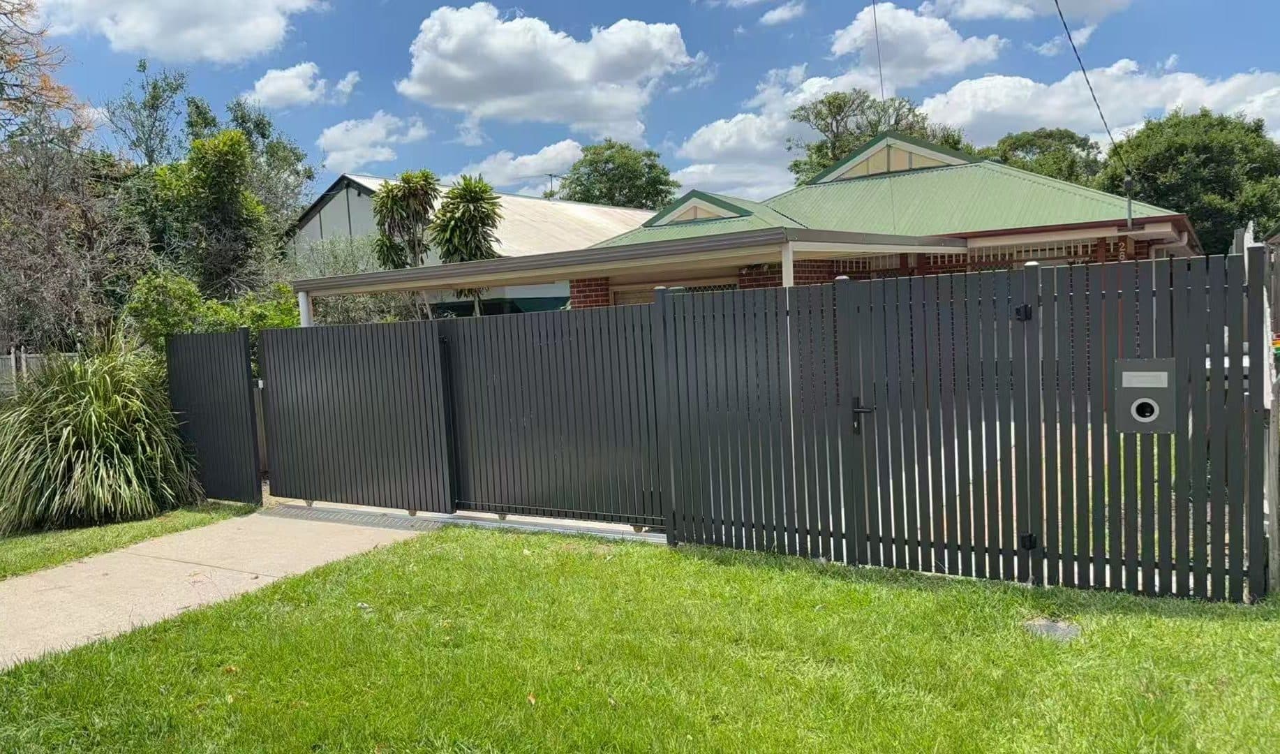 Monument aluminium vertical picket fence with pedestrian gate, letterbox and sliding gate along a front lawn