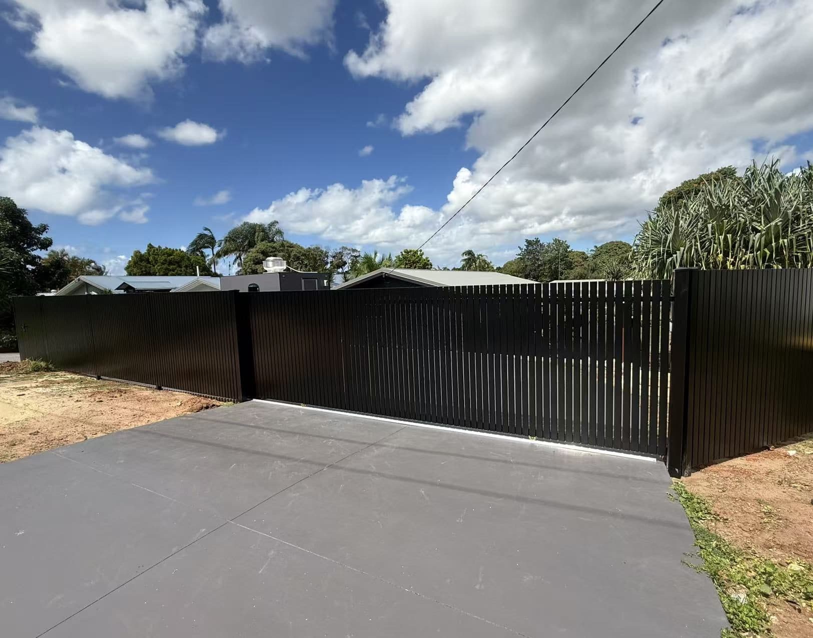 Black aluminium vertical picket sliding driveway gate and fence across a new concrete driveway
