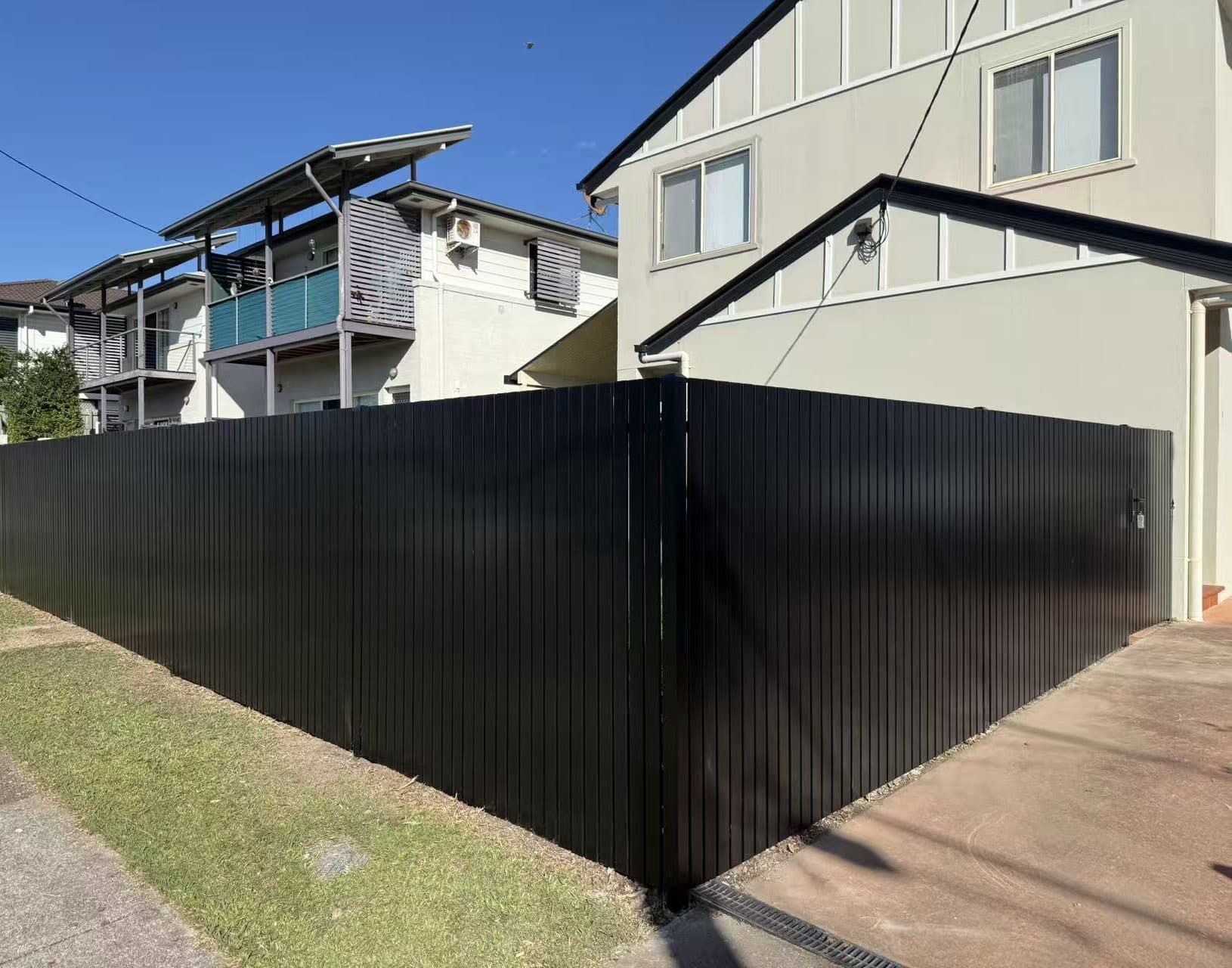 Black aluminium vertical picket fence wrapping a corner between the footpath and a driveway