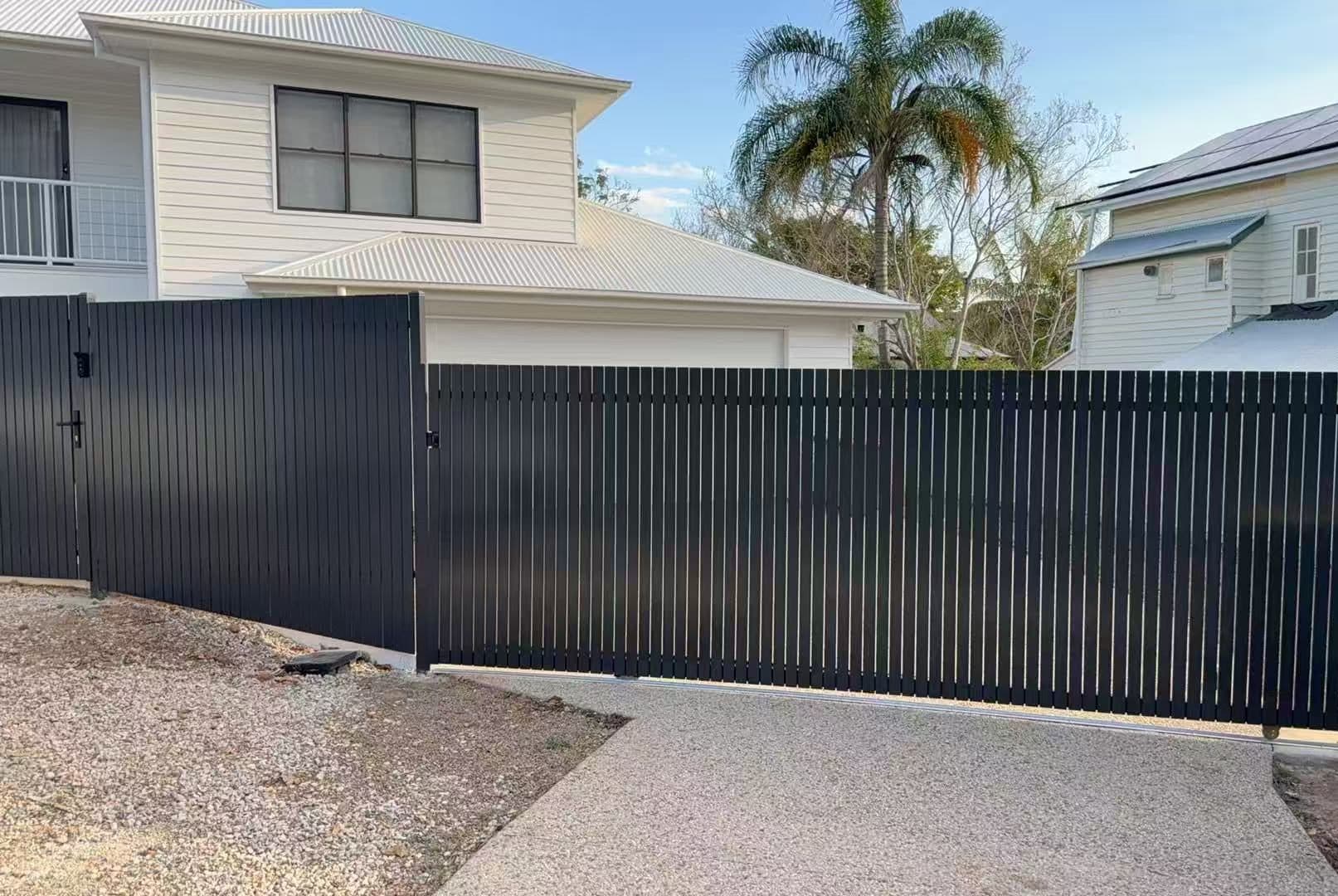 Dark grey aluminium vertical picket sliding driveway gate, fence and pedestrian gate across an aggregate drive