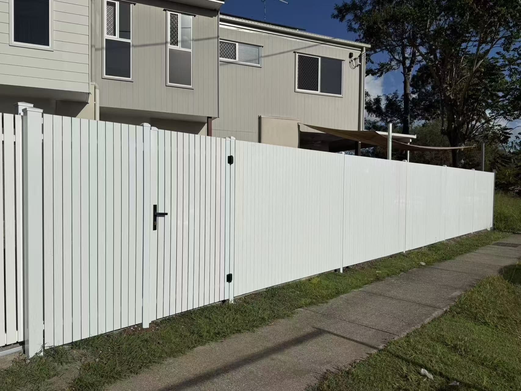 White aluminium vertical picket fence with a flush pedestrian gate along a footpath boundary