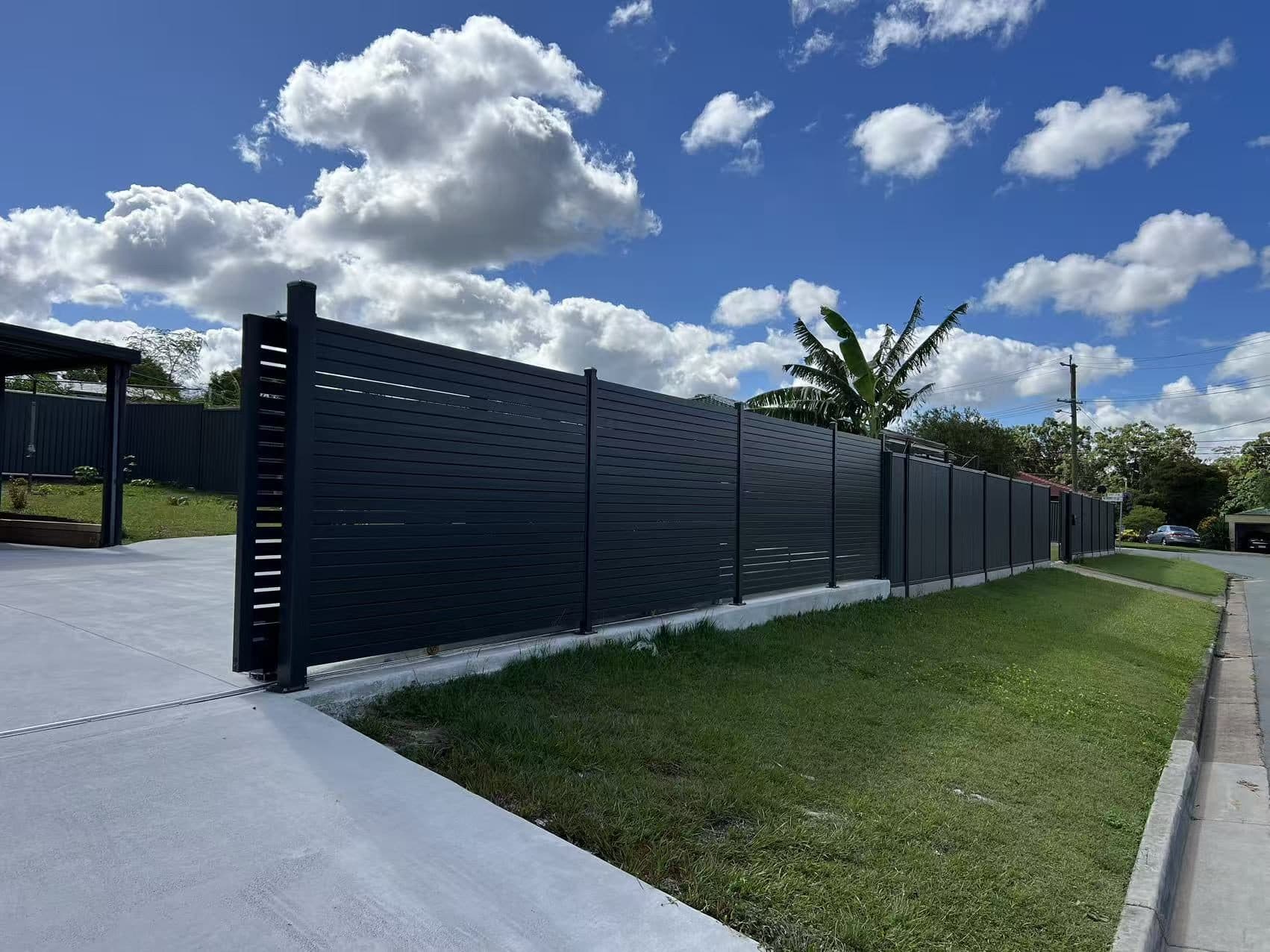 Dark grey aluminium horizontal slat fence on a concrete plinth along a front boundary beside a new driveway