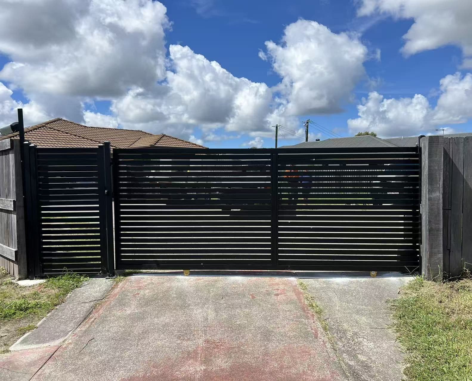 Black aluminium horizontal slat sliding driveway gate and pedestrian gate between timber boundary fences