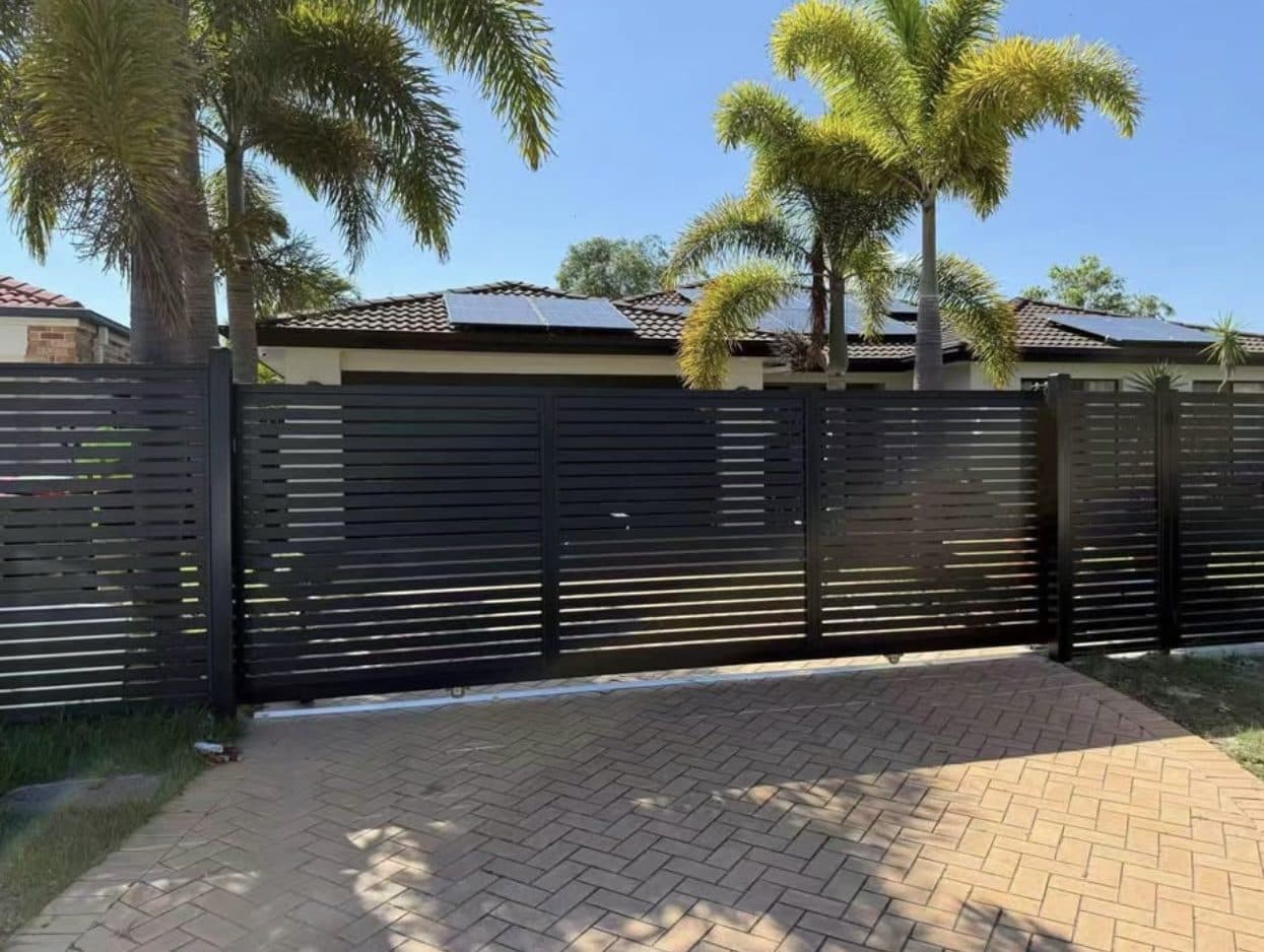 Black aluminium horizontal slat sliding driveway gate and fence across a herringbone paved driveway
