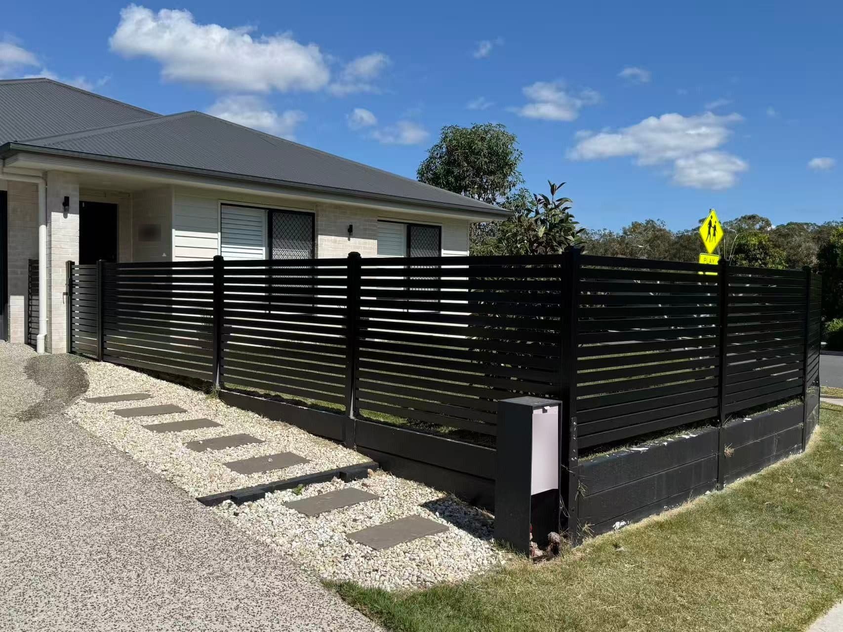 Black aluminium horizontal slat fence on a plinth, with a letterbox post, around the front garden of a corner home